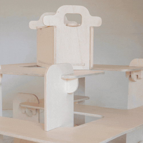 Light wood toy construction with a central pillar, horizontal arms, and a box on top on a tabletop.