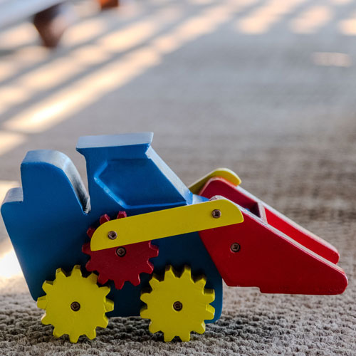 Colorful wooden toy dump truck with blue cab, red cargo bed, yellow wheels on a carpet.