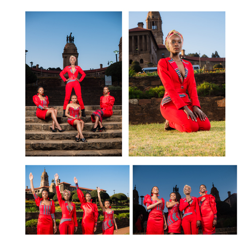 Group of five women wearing red outfits posing on stone steps with a historic monument and blue sky in the background.