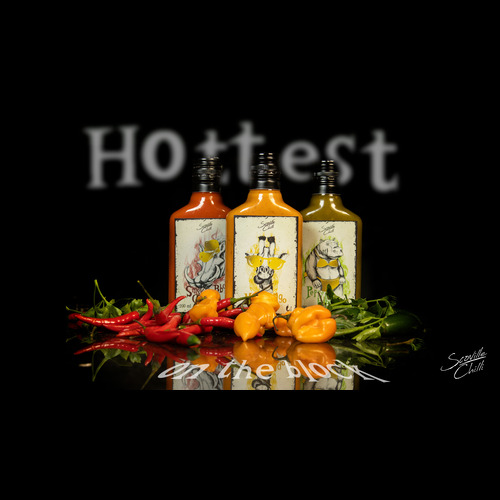 Studio shot of three hot-sauce bottles (red, orange, and green) with chili peppers on a glossy black surface.