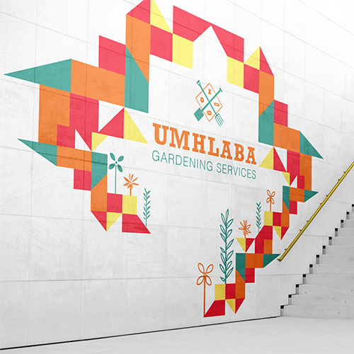 Colorful geometric mural around a central UMHLABA GARDENING SERVICES logo painted on a white wall beside a staircase.