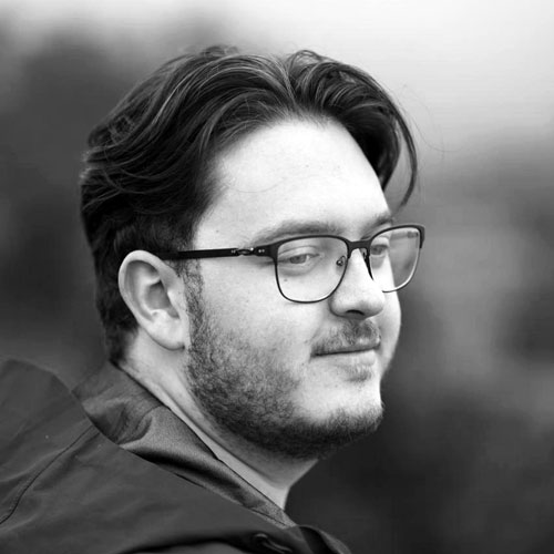 Black-and-white portrait of a man with glasses in profile, looking to the right outdoors.