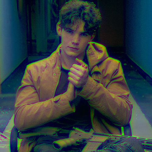 Young man in a brown jacket sits in a dim hallway, facing the camera, with a pistol and ammo on his lap.