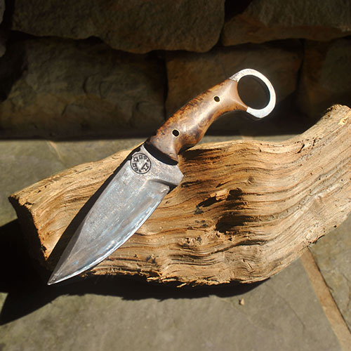 Fixed-blade knife with a wooden handle resting on a split log, outdoors on a stone surface.
