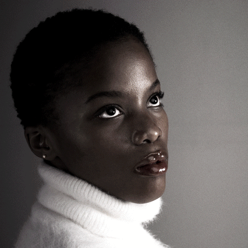 Portrait of a Black woman in a white turtleneck looking upward, studio lighting on one side of the face.