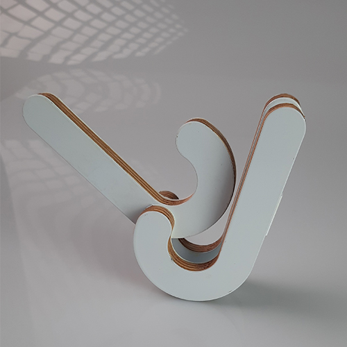 White interlocking wooden sculpture forming a stylized W on a pale surface, with visible plywood edges and soft shadow pattern.